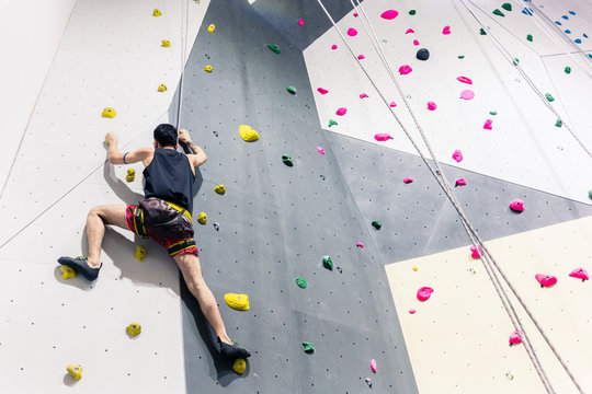 Rear view of man climbing wall with help of grip
