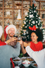 Friends drinking alcohol and having dinner for Christmas eve at home. Christmas holidays concept.