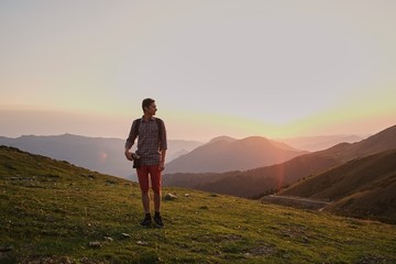 Obraz premium man with a camera walks alone on a mountain road in the background of the sunset