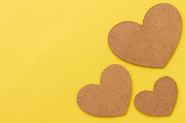 Fototapeta premium Yellow paper background with three brown wooden hearts. Cardboard concept for Valentine's Day. Backdrop for Valentine's Day.