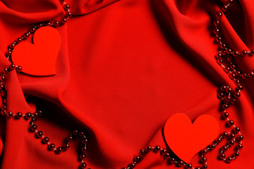 Two red hearts on a red drapery fabric with red shiny beads. Cropped shot, horizontal, place for text, background. Valentine's day concept