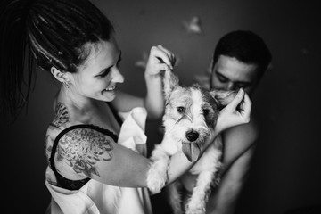 Young positive hipster couple holding a shaggy dog in their hands, who stuck out his tongue. Jack Russell Terrier.