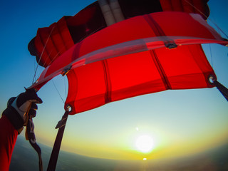 Skydiver's red and black open parachute sailing toward the sun