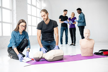 Fototapeta premium Group of young people practising to make artificial breathing with medical dummies during the first aid training in the white room