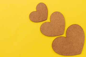Three wooden brown hearts on a yellow cardboard background with place for text. Concept for valentine's day. Background about love and tenderness.