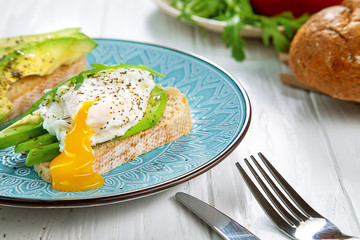 Tost with avocado and poached egg on a blue plate. Fresh and healthy breakfast with avocado toast and orange juice with a book. Healthy food. Morning breakfast. Copy space for text, logo or brand.