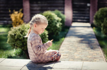 Baby girl with long hair and beautiful dress sits on the doorstep at home and looks at a little doll