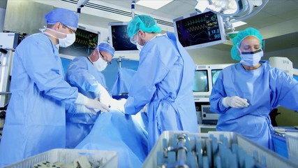 Surgical healthcare medical training team in scrubs working in modern hospital operating theater facility performing Orthopaedic surgery on patient 