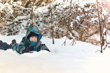Fototapeta na wymiar Happy smiling boy lying in the snow in the winter forest.