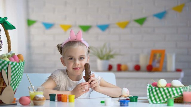 Little girl in cute headband smiling and posing at camera with chocolate bunny