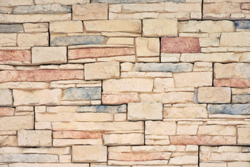 Background with old brick wall of aged beige and colorful bricks. Natural stone surface with rough texture and selective focus. Decorate abstract wallpaper with structure granite rocks.