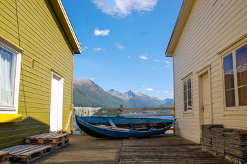 Old little blue boat and a fishing net in picturesque and colorful Norwegian town scenery; fjord background