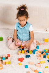 high angle view of cute african american child sitting on carpet and playing with colorful wooden blocks