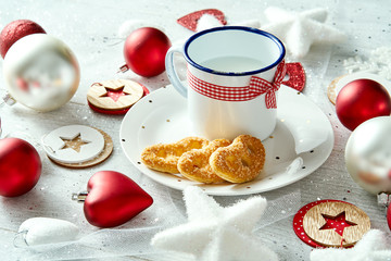 Christmas decoration with a mug of milk plate with gingerbreads snowflakes and baubles on a white silvery table.