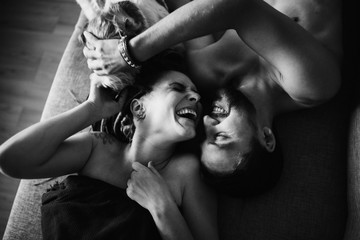 Young beautiful couple are lying on the couch and laughing. Dog sniffs them. selective focus. top view