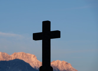 Silhouette of crucifix cross and Catholic background with  mountain peaks  at sunset.