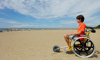 boy  sitting on the special wheelchair with aluminum alloy wheels on the beach