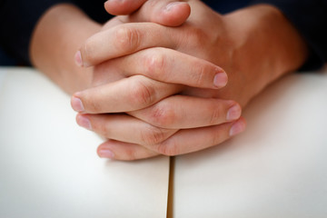 Hands folded in prayer on a Holy Bible in church concept for faith, spirtuality and religion