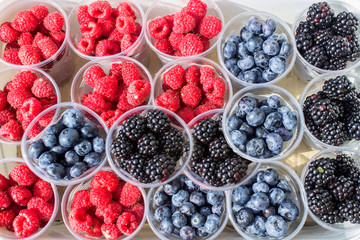 Blueberries strawberries and raspberries in plastic cups.