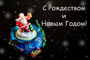 Cute toy Santa Claus isolated on black background with white inscription on Russian language with snowflakes
