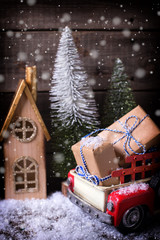 Wrapped boxes in red car, houses and fur trees   on aged wooden background.