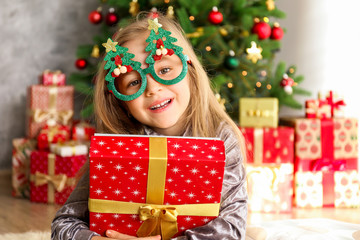 Portrait of cute happy five year old girl receiving many presents, Decorated Christmas tree with stack of wrapped gifts on background. Close up, copy space.