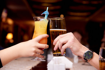 Female hand with a cocktail and male hand with beer close-up.