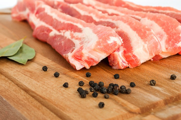 Fresh raw bacon slices on a brown wooden chopping board, selective focus closeup