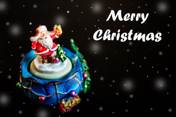 Cute toy Santa Claus isolated on black background with snowflakes and white inscription merry christmas