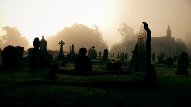 Old spooky graveyard with morning mist and church in the distance