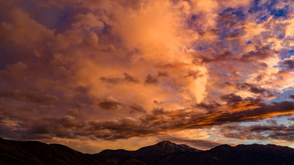 Aerial, drone view of sunrise before a storm with beautiful, vivid and vibrant colors of gold, purple, blue and orange over Mount San Gorgonio in the San Bernardino Mountains with white snow