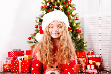 Obraz na płótnie Canvas Portrait of cute happy nine year old girl wearing red christmas sweater with many presents, Decorated Christmas tree with stack of wrapped gifts on background. Close up, copy space.