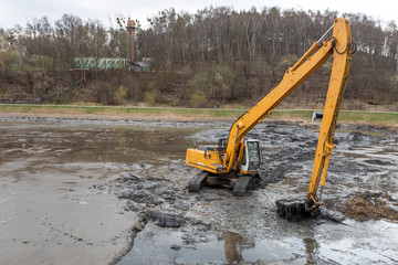 Yellow excavator while working in the mud