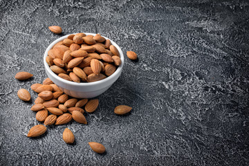 Healthy whole almonds in white bowl on dark concrete