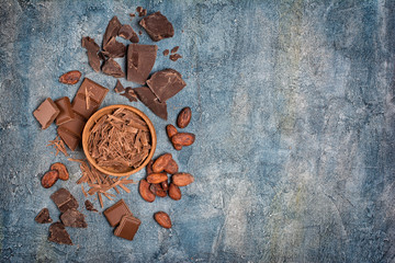 .Top view of chocolate chips in wooden bowl with pieces of chocolate bar and cocoa beans