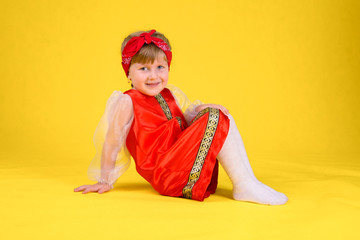 The child shows the class and sits on the splits. Yellow background. Girl with long hair in a stylized red dress