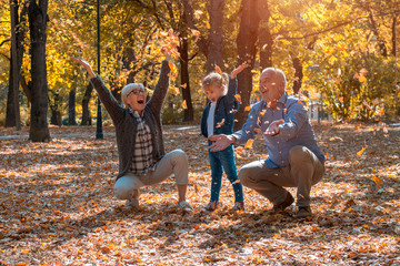 Grandparents and granddaughter throwing leaves in park and having fun together