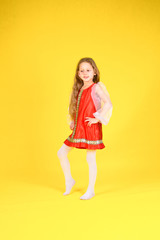 The child shows the class and sits on the splits. Yellow background. Girl with long hair in a stylized red dress