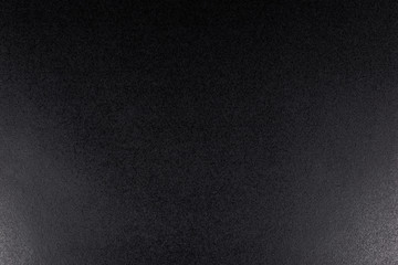 Black, rough textured background lit with dim light.