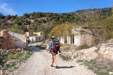 A girl with large backpack walks through the ruins of an abandoned Turkish village in Cyprus