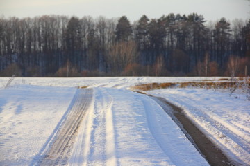 Fototapeta na wymiar Beautiful rural dirt road under snow with sunbeams, track in a field with forest on the horizon - rural landscape, travel