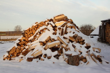 Preparation in winter, wood - a large pile of chopped firewood under the snow in the backyard of...