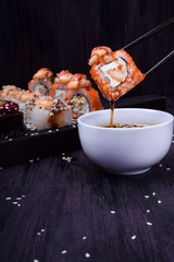Sushi roll is dipped into the bowl with soy sauce against the dark background