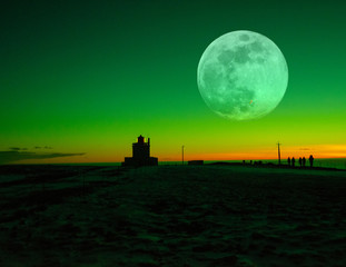 Lighthouse silhouette with green sky and Large Moon. 