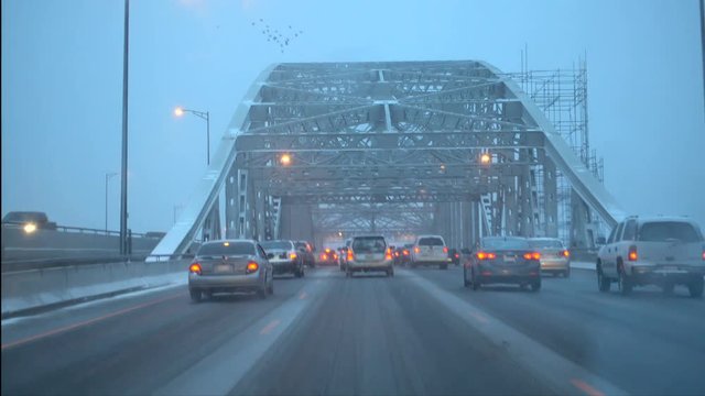 Crossing Burlington Bay Skyway bridge in snowy winter. Slow moving heavy traffic jam on the bridge with snow causing hazardous conditions on overcast day. Slush covered road bridge is dangerous.