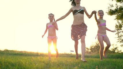 Young mother plays with her daughters on green grass. Older sister runs with younger sisters in the park. Happy family enjoying nature at sunset. Only women. Feminism. Slow motion