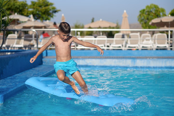 Naklejka premium Boy having fun in swimming pool at hotel. He making jump from inflatable mattress into water.