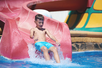 European kid is having fun in the waterpark. He is gliding from the water slide.
