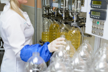 line of production of refined sunflower oil. Girl worker at a factory on a conveyor background with...