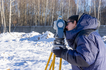 Topographer makes geodetic survey of the construction site for the inventory in winter